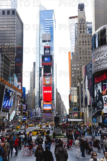 USA, New York, New York City, Manhattan  People walking in Times Square at the junction of 7th Avenue and Broadway below buildings with advertising on large video screens.