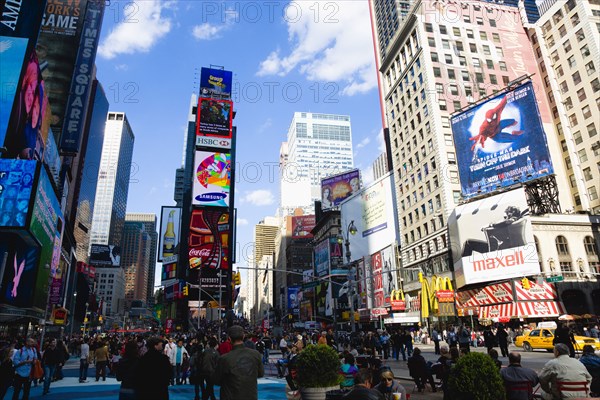 USA, New York, New York City, Manhattan  People walking in Times Square at the junction of 7th Avenue and Broadway below buildings with advertising on large video screens with yellow taxi cabs driving down 7th Avenue.