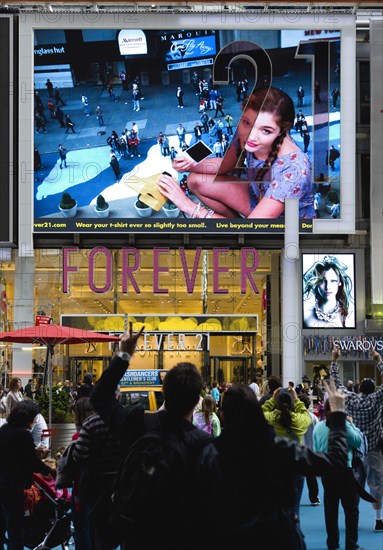 USA, New York, New York City, Manhattan  People waving and looking at themselves in a giant live real time TV video LED screen in Times Square above Forever 21 clothing shop.
