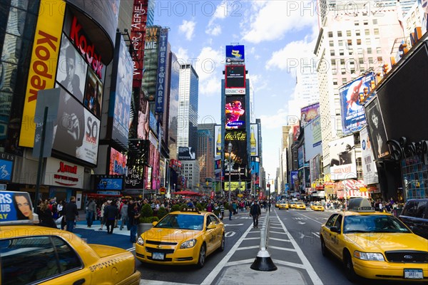 USA, New York, New York City, Manhattan  People walking in Times Square at the junction of 7th Avenue and Broadway below buildings with advertising on large video screens with yellow taxi cabs driving down 7th Avenue.