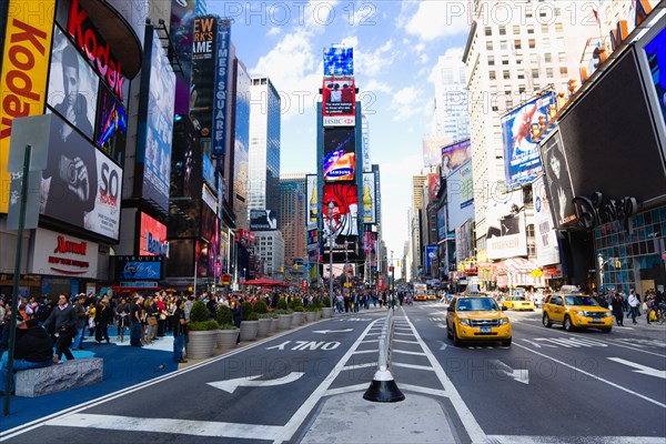 USA, New York, New York City, Manhattan  People walking in Times Square at the junction of 7th Avenue and Broadway below buildings with advertising on large video screens with yellow taxi cabs driving down 7th Avenue.