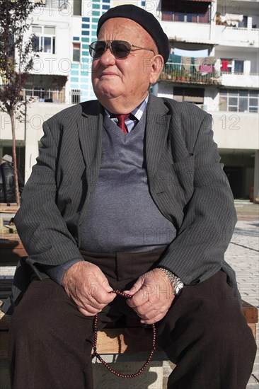Albania, Tirane, Tirana, Three-quarter portrait of an elderly man wearing black beret and sunglasses  seated  turned to left  and holding prayer beads.