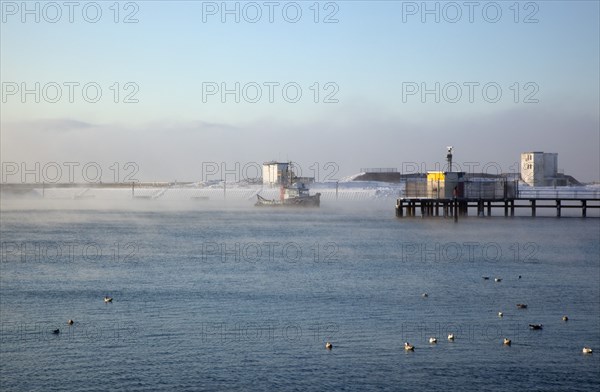 England, West Sussex, Shoreham-by-Sea , Mist rising from harbour waters on frosty morning with tug boat on the river