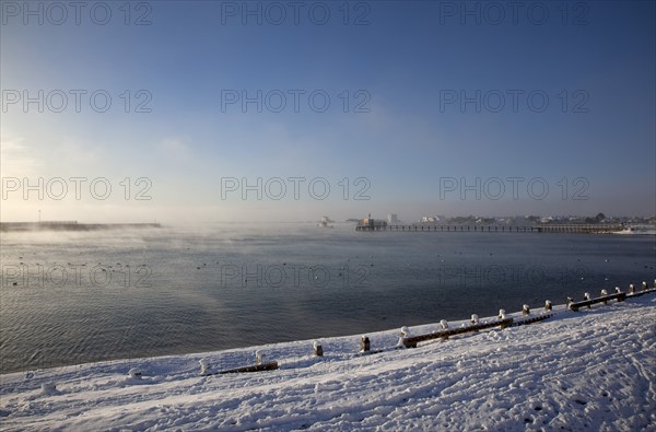 England, West Sussex, Shoreham-by-Sea , Mist rising from harbour waters on frosty morning with snow on the beach.