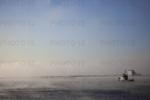 England, West Sussex, Shoreham-by-Sea , Mist rising from harbour waters on frosty morning with tug boat on the river Adur.