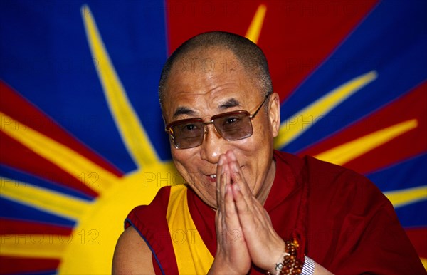 China, Tibet, Religious, The Dalai Lama smiling with hands raised in a traditional anjali greeting gesture.  Vibrant image of a yellow sun in the background.