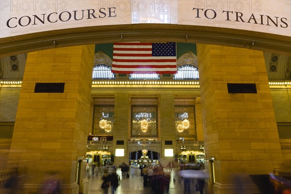 USA, New York, New York City, Manhattan  Grand Central Terminal railway station entrance to the Main Concourse from the Vanderbilt Hall with people walking below the American Stars and Stripes flag hanging from the ceiling.