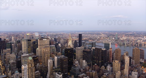 USA, New York, New York City, Manhattan  View from Empire State building over midtown skyscrapers and East River towards Queens and Long Island with Art Deco Chrysler Building illuminated at dusk.