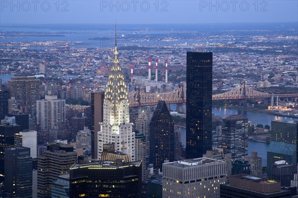 USA, New York, New York City, Manhattan  View from Empire State building over midtown skyscrapers and East River towards Queens and Long Island with Art Deco Chrysler Building and Queensboro Bridge illuminated at sunset.