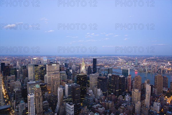 USA, New York, New York City, Manhattan  View from Empire State building over midtown skyscrapers and East River towards Queens and Long Island with Art Deco Chrysler Building illuminated at sunset.