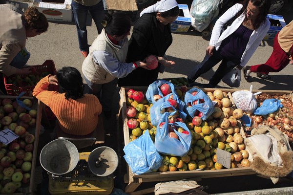 Albania, Tirane, Tirana, Looking down on stall of street vendor selling apples  pomegranates and onions sitting beside set of scales with female customers making purchases.