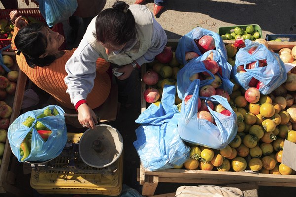 Albania, Tirane, Tirana, Looking down on street vendor using set of scales to weigh chillis at stall with display including apples and pomegranates.