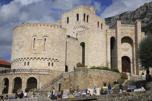 Albania, Kruja, Kruja Castle and Skanderbeg Museum exterior with tourist visitors and souvenir stalls in foreground.