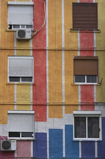 Albania, Tirane, Tirana, Detail of exterior facade of striped  multi-coloured apartment block with windows  window blinds and air conditioning units.