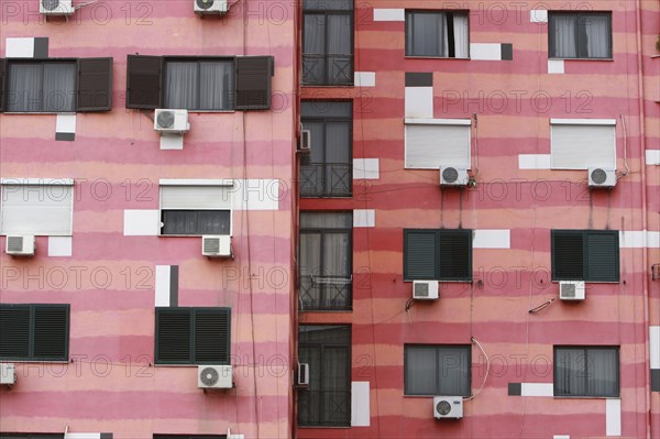 Albania, Tirane, Tirana, Part view of pink striped exterior facade of apartment building with air conditioning units.