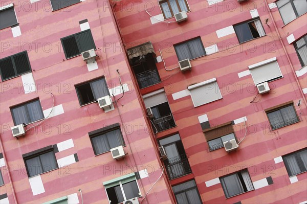 Albania, Tirane, Tirana, Angled part view of pink striped exterior facade of apartment building with air conditioning units.