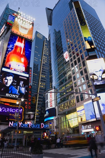 USA, New York, New York City, Manhattan  People walking at night in Times Square at the junction of 7th Avenue and Broadway by the New York Police Department station below buildings with advertising on large video screens.