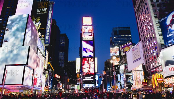 USA, New York, New York City, Manhattan  People walking at night in Times Square at the junction of 7th Avenue and Broadway below buildings with advertising on large video screens.