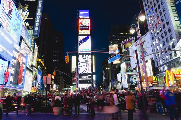 USA, New York, New York City, Manhattan  People walking at night in Times Square at the junction of 7th Avenue and Broadway below buildings with advertising on large video screens.