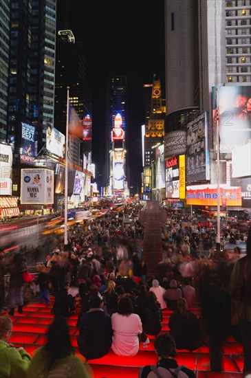 USA, New York, New York City, Manhattan  People sitting on lit red steps or walking at night in Times Square at the junction of 7th Avenue and Broadway below buildings with advertising on large video screens.