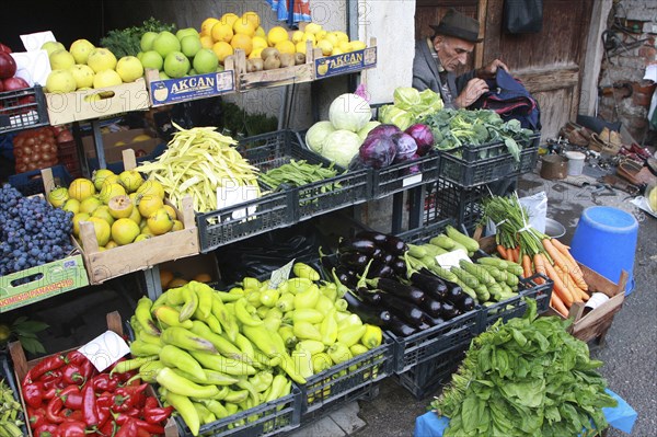 Albania, Tirane, Tirana, Display of fruit and vegetables including peppers  cabbage and grapes at grocers shop in the Avni Rustemi market. Shoe mender in doorway at side.