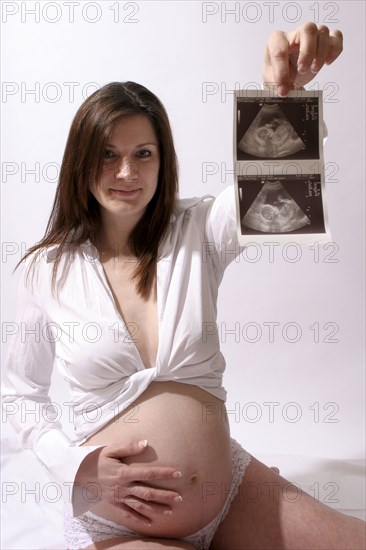Health, Pregnancy, Scan, Young  pregnant woman holding up her ultrasound scan photograph with one hand  the other resting on her stomach.