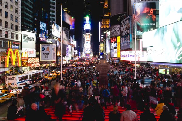 USA, New York, New York City, Manhattan  People sitting on lit red steps or walking at night in Times Square at the junction of 7th Avenue and Broadway below buildings with advertising on large video screens.