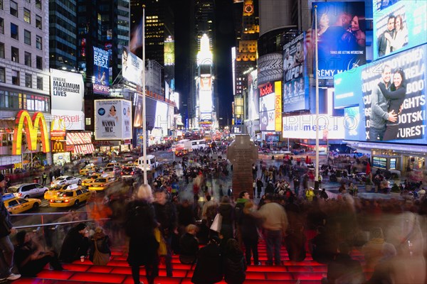 USA, New York, New York City, Manhattan  People sitting on lit red steps or walking at night in Times Square at the junction of 7th Avenue and Broadway below buildings with advertising on large video screens.