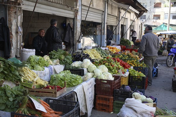 Albania, Tirane, Tirana, Customer and vendors at fruit and vegetable stalls in the Avni Rustemi market with display including carrots  lettuce  aubergines  peppers and oranges.