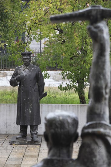 Albania, Tirane, Tirane, Statue of Stalin standing opposite another statue of figure standing with arm raised  holding a pick axe  in foreground seen from behind.