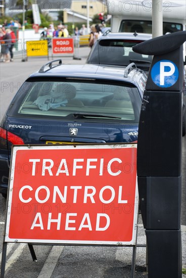 England, West Sussex, Bognor Regis, Solar panel powered Pay & Display parking meter on the sidewalk pavement for on street parking beside red Traffic Control Ahead sign with parked cars and a Road Closed and Diversion signs in the distance.