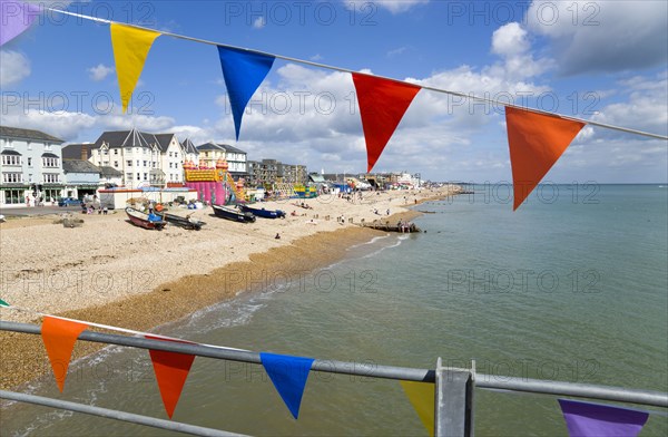 England, West Sussex, Bognor Regis, The pebble shingle beach and seafront with tourists seen through colourful flags hanging from the pier.