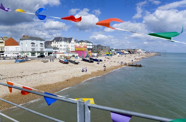 England, West Sussex, Bognor Regis, The pebble shingle beach and seafront with tourists seen through colourful flags hanging from the pier.