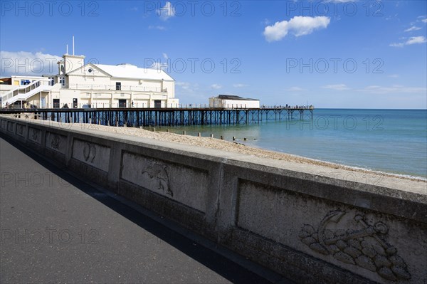 England, West Sussex, Bognor Regis, The Pier with people fishing off the end and the shingle pebble beach and the promenade with sea defence wall.