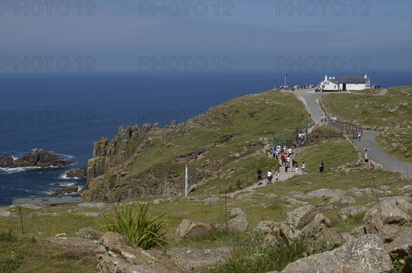 England, Cornwall, Lands End, View over the most western point of mainland Britain with visitors walking along coastal path toward small white building