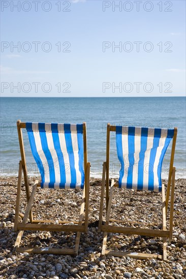 England, West Sussex, Bognor Regis, Two blue and white deck chair on the shingle pebble beach looking out to sea.