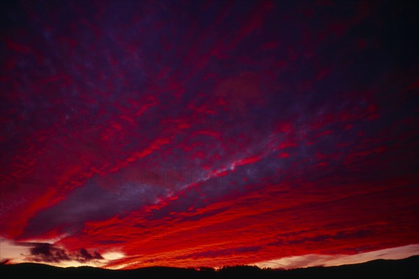 England, Climate, Sunset, Narrow  strip of land silhouetted against dramatic sunset sky with clouds lit red  pink  orange and purple.