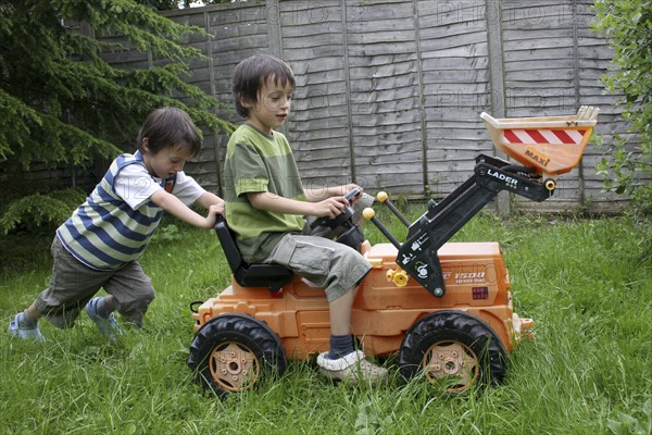 Children, Playing, Outdoors, Two twin boys aged six years old playing outside in a garden on a toy tractor.