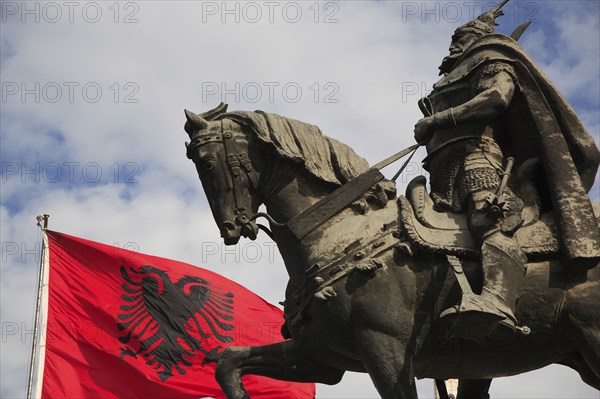 Albania, Tirane, Tirana, Skanderbeg Square. Part view of equestrian statue of national hero George Castriot Skanderbeg also known as The Dragon of Albania beside red flag with double headed eagle emblem.