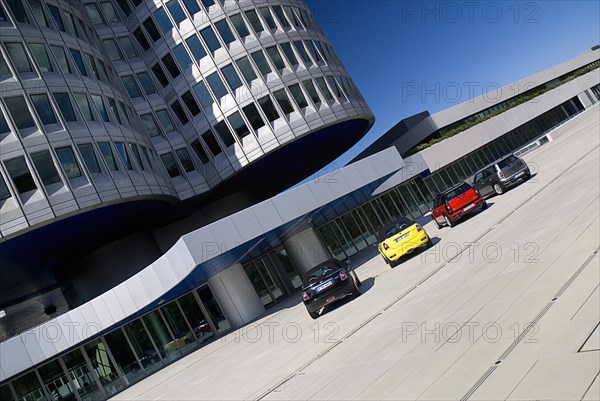 BMW Headquarters exterior. The BMW Tower which stands 101 metres tall and mimics the shape of tyres. Angled part view of tower base with minis parked in foreground. Photo : Hugh Rooney