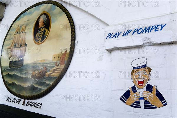 Wall paintings outside a tattooist parlour underneath railway arches at Portsmouth Harbour Station showing a sailor with the local football club slogan Play Up Pompey and an old painting of Admiral Lord Nelson and the harbour. Photo : Paul Seheult
