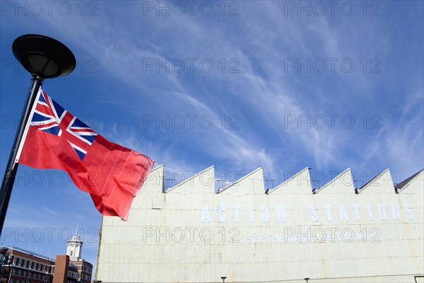 Historic Naval Dockyard Red Ensign merchant marine flag flying from flagpole with Action Stations exhibition sign on building. Photo: Paul Seheult