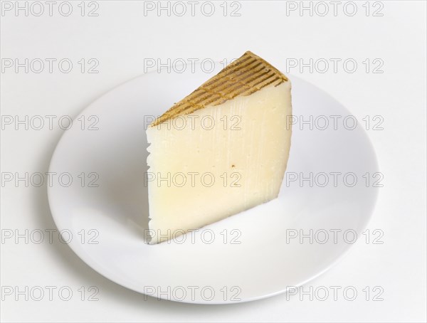 Slice of Spanish Manchego cheese made from pasteurised Manchega sheeps milk from the La Mancha region of Spain on a plate against a white background. Photo : Paul Seheult