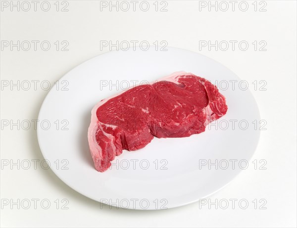 Slice of raw uncooked sirloin steak on a round white plate against a white background. Photo : Paul Seheult