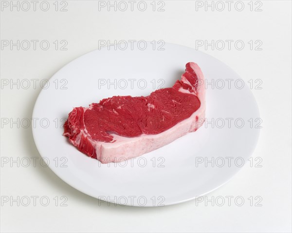 Slice of raw uncooked sirloin steak on a round white plate against a white background. Photo : Paul Seheult