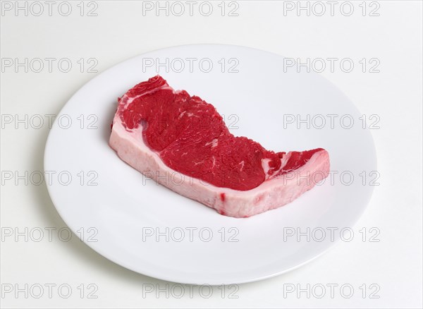 Slice of raw uncooked sirloin steak on a round white plate against a white background. Photo : Paul Seheult