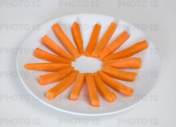 Slices of raw uncooked carrot on round white plate against a white background. Photo : Paul Seheult