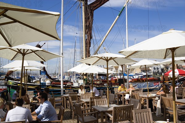 Port Solent People at restaurant tables under sun shade umbrellas with yachts moored in the marina and housing beyond. Photo: Paul Seheult