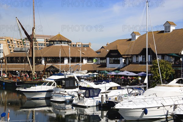 Port Solent Boats moored in the marina with people sitting at restaurant tables beyond beside a pub and housing apartments. Photo: Paul Seheult
