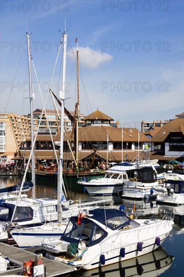 Port Solent Boats moored in the marina with people sitting at restaurant tables beyond beside a pub and housing apartments. Photo : Paul Seheult